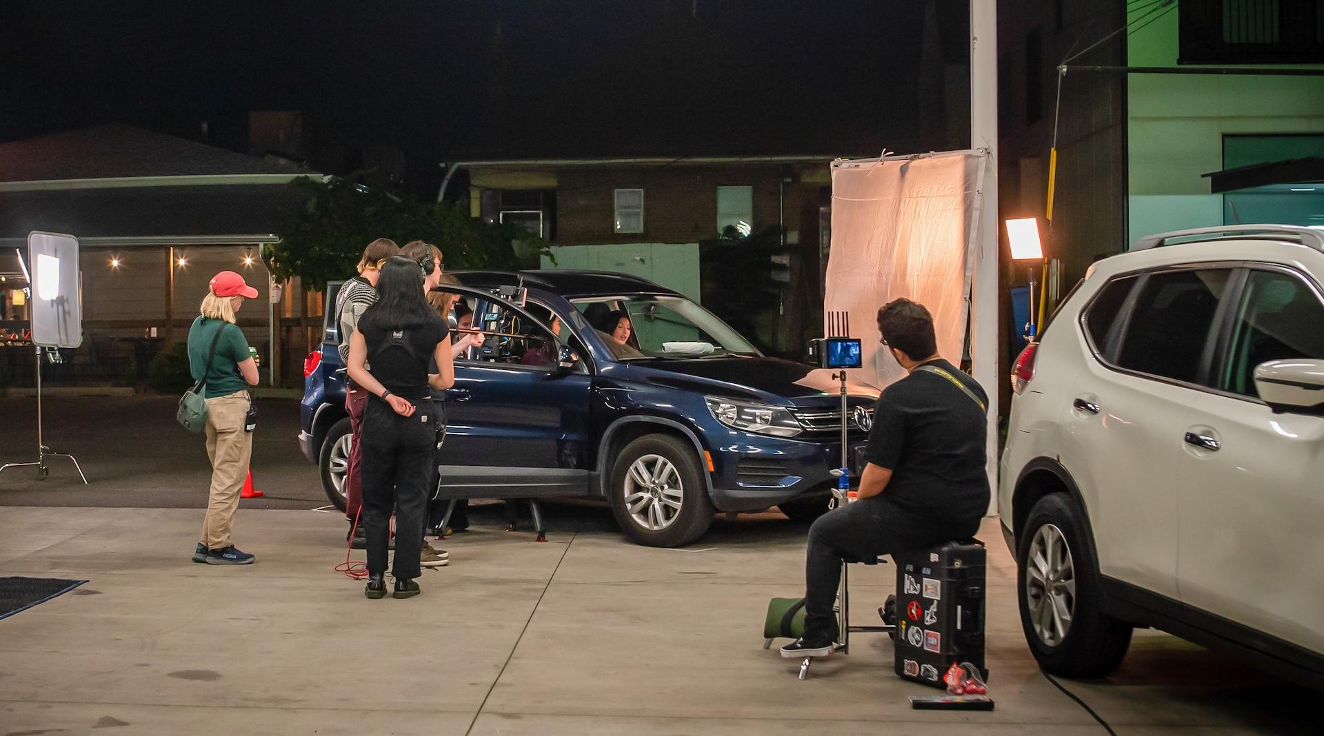 Phase 2 fellows surround a car with lighting and camera gear at night, under what appears to be a covered parking structure.