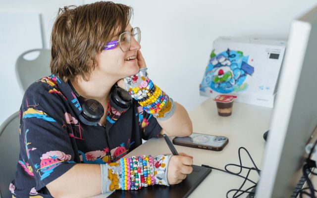 student sits in front of a computer, smiling